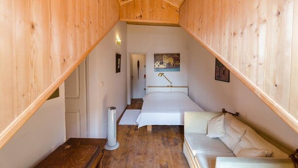 Una habitación pequeña y acogedora con una cama, un sofá y un calefactor en el suelo.