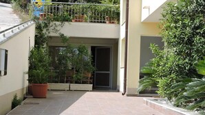 Un patio con suelo de baldosas, plantas en macetas y una puerta que da a un edificio.