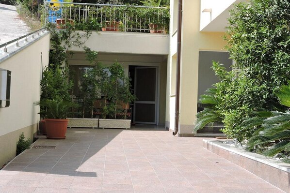 Une cour avec un sol carrelé, des plantes en pot et une porte donnant accès à un bâtiment.