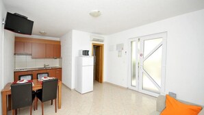 Un espacio habitable compacto con kitchenette, comedor y sofá con cojín naranja.