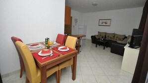 Comedor con mesa de madera preparada para cuatro personas, sillas amarillas y un mantel individual rojo. Se ve una cocina al fondo con un refrigerador blanco y un microondas.