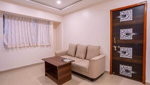 A living room with a beige sofa, a wooden coffee table, a window with curtains, and a door with decorative panels. - Treebo Royal Comfort Atithi (Pune)