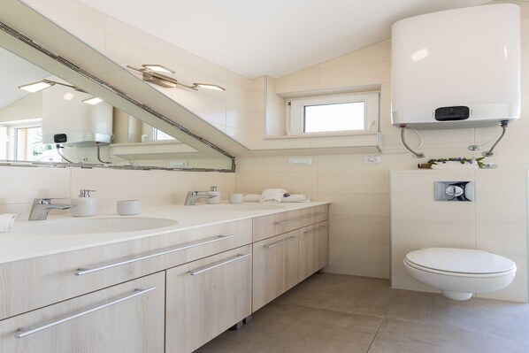 Un baño moderno con un espejo grande, dos lavamanos, un inodoro y un calentador empotrado.