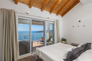Un dormitorio con una cama grande, un balcón con vistas al mar y un techo de madera.
