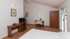 A bedroom with a bed, a wooden desk with a television, a dining table with chairs, and a wardrobe.