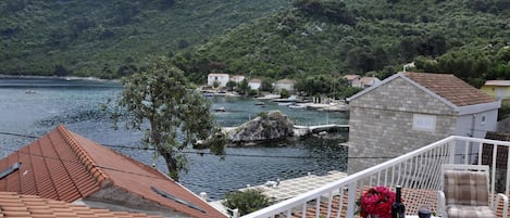 A terrace with a table set for two, overlooking a lake with boats and houses in the background.