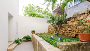 A narrow courtyard with a stone wall, potted plants, and a small garden area. - Miracle Apartments - Studio Apartment with Terrace and City View (Dubrovnik)