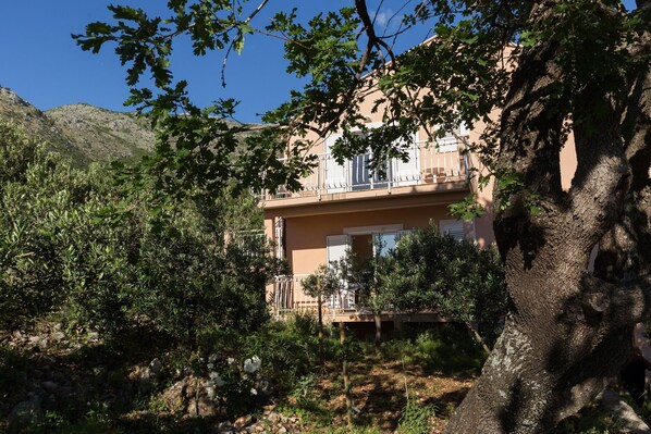 Un edificio di due piani con balconi, circondato da alberi e con montagne sullo sfondo.