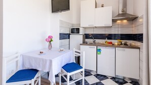 Een functionele keuken met witte kastjes, een magnetron, een spoelbak en een kleine eethoek met een tafel en stoelen.