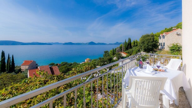 A terrace with white chairs and a table set for dining, overlooking a body of water and distant mountains. - Apartments Cypress Sea Cove - Comfort Studio Apartment with Balcony and Sea View (A1) (Slano)