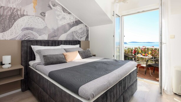 Une chambre avec un grand lit, une table de chevet, une fresque murale et un balcon équipé d’une table et de chaises.