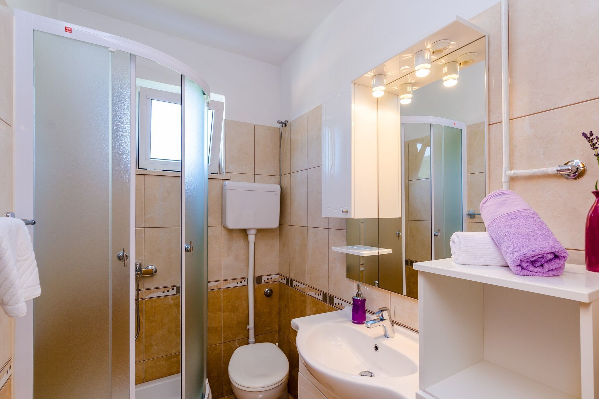 A bathroom with a toilet, shower, sink, and a mirror with lights.