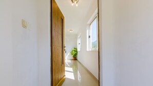 A hallway with a wooden door, a potted plant, and a window.