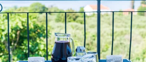 Een tafel gedekt met een waterkan, bekers en suikerpotten op een balkon met uitzicht op groen en bergen.