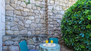 A stone wall with a small table and chairs, two glasses of orange juice, and a green bush. - Villa Alegria Cavtat - Studio Apartment with Patio and Garden View (Cavtat)