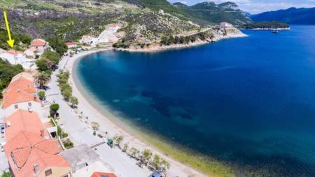 A coastal town with a beach, houses with red roofs, and a mountainous backdrop.