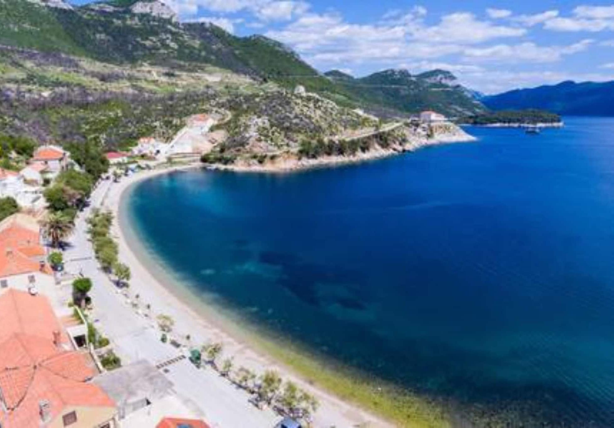 Une ville côtière dotée d’une plage, de maisons aux toits rouges et bordée par une chaîne de montagnes.
