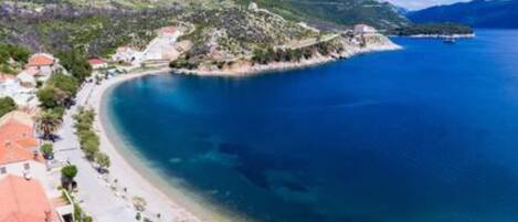 Un pueblo costero con playa, casas de techo rojo y montañas al fondo.