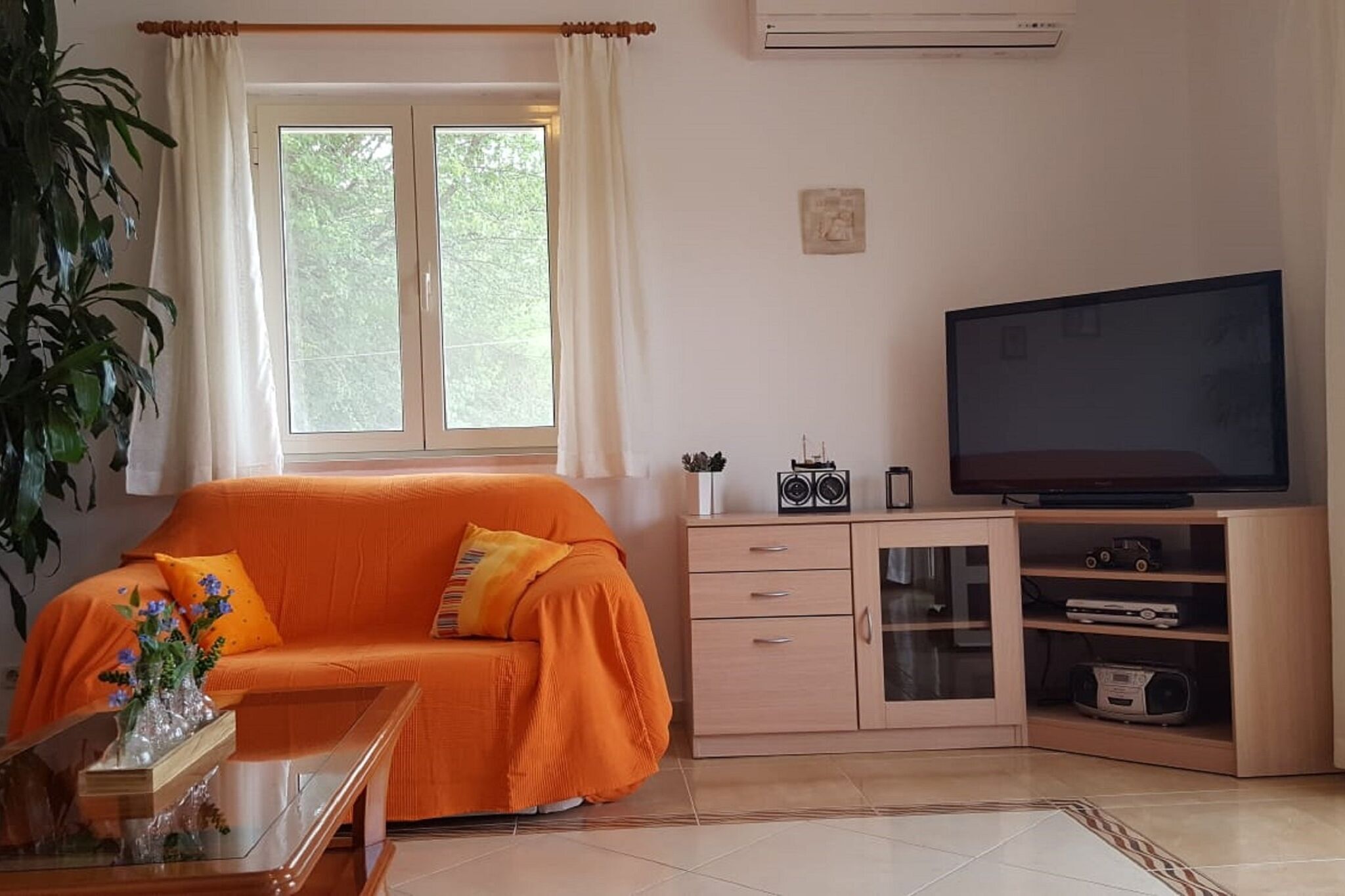 Ein Wohnzimmer mit einer Couch, einem Fernseher, einem Schrank und einem Fenster mit Vorhängen.