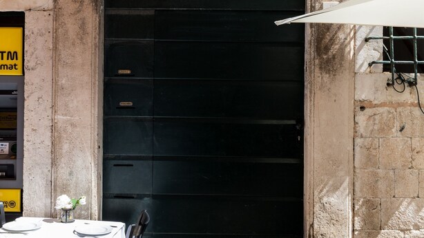 A closed black door with a small window, a table with plates and a vase of flowers, and a yellow sign with 'TM' on it.
