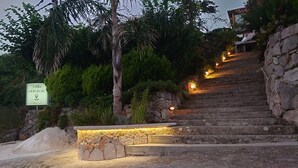 Un escalier en pierre mène à la villa Peraglio, qui est entourée d’une végétation luxuriante et illuminée par des lumières chaleureuses.