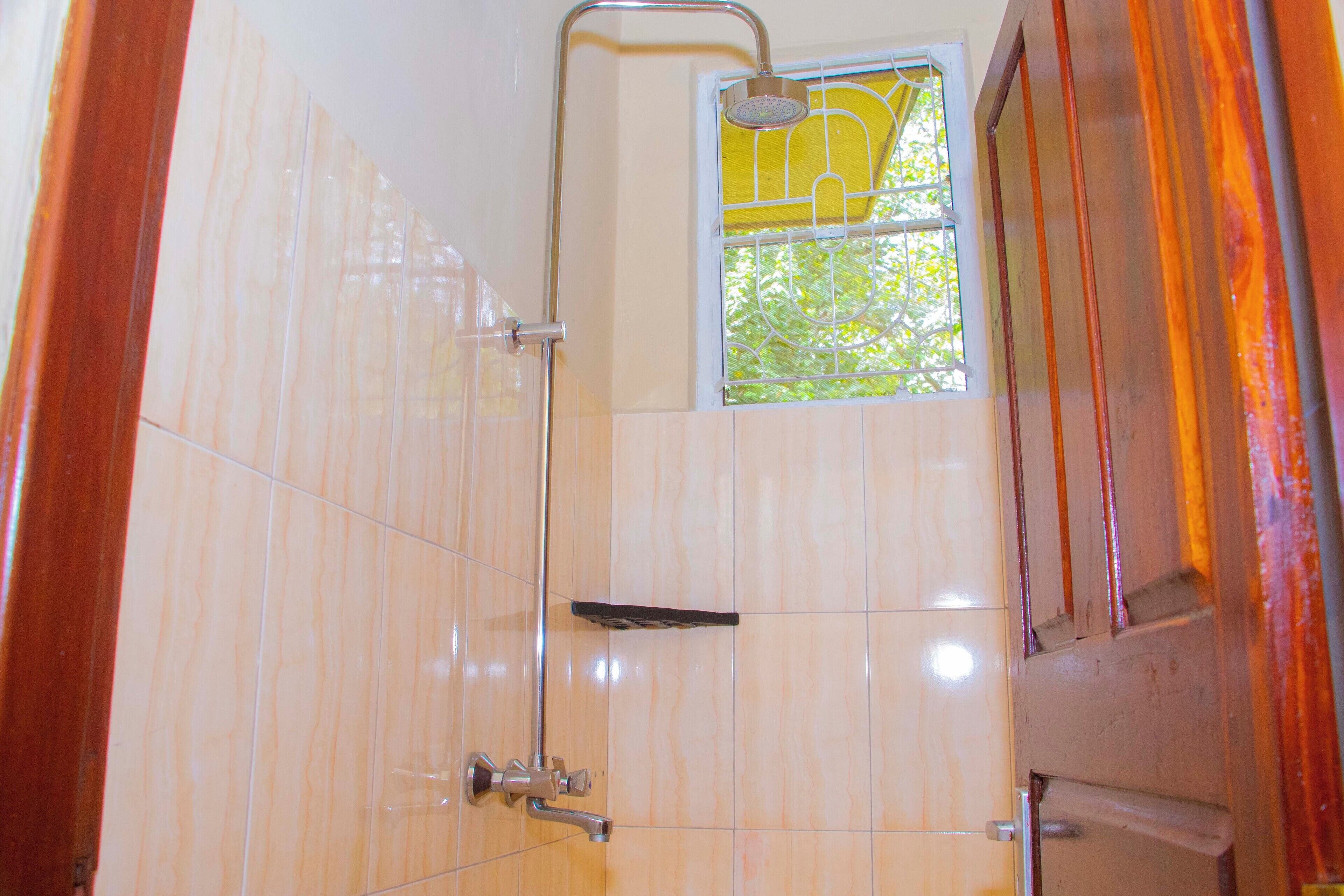 A bathroom with a shower, a window with a view of trees, and a wooden door.
