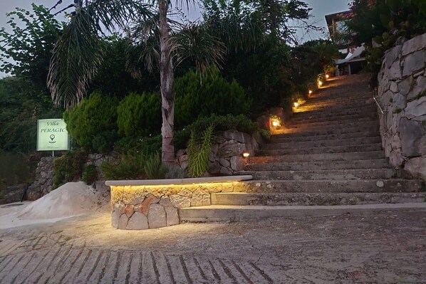 A stone staircase leading to Villa Peraglio, surrounded by lush greenery and illuminated by warm lights.