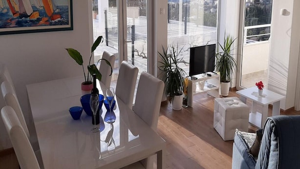 A modern living room with a dining area, large windows, and a city view. - Villa Nika-Five Bedroom Villa with Pool (Mlini)