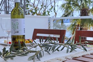 A bottle of Vina Papak ILOK Radosh wine, a glass, and a plate with fruits on a table outdoors.