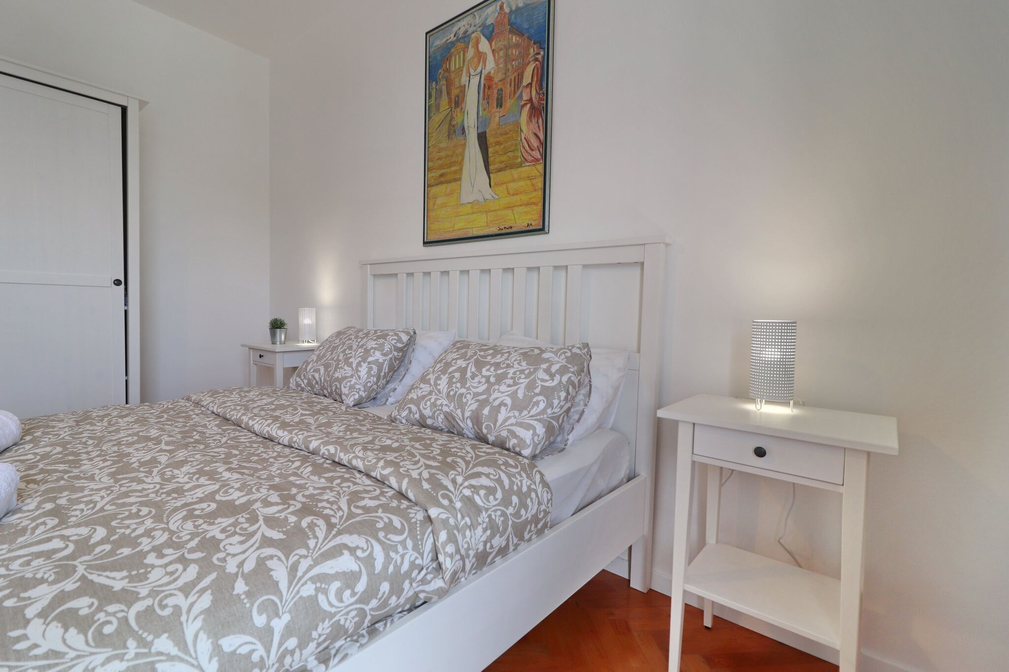 Une chambre à coucher avec un lit, une table de chevet blanche et un tableau accroché au mur.