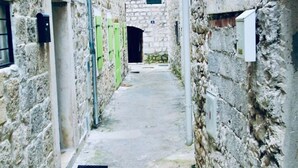 A narrow stone corridor with a rough texture, leading to a doorway.