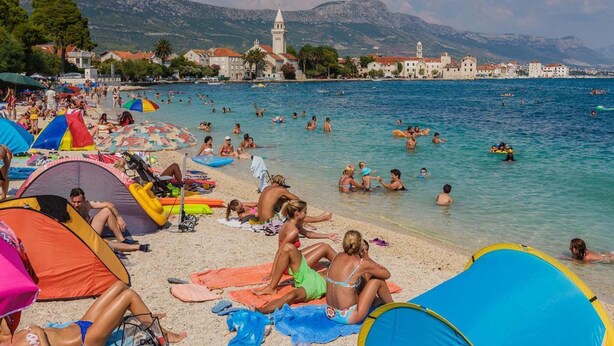A beach with tents, people swimming, and a historic building in the background.