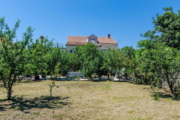 A house with a red-tiled roof, surrounded by a garden with various trees and a clear blue sky. - Villa Ro-Ma - Three Bedroom Villa with Terrace and Sea View (Slano)