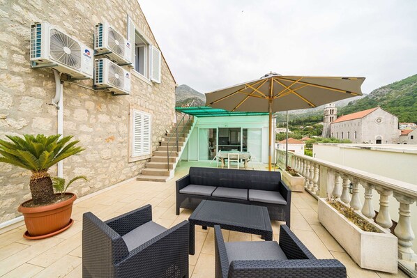 Un balcon aménagé avec du mobilier d’extérieur, un pot de fleurs et des unités de climatisation installées sur la façade de l’immeuble.
