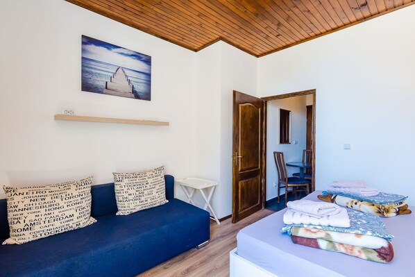 Una habitación con un sofá azul, techo de madera, un cuadro de un muelle, una puerta de madera y una cama con mantas.