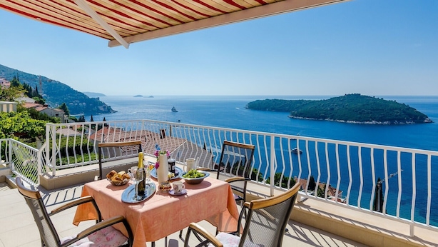 A terrace with a table set for dining, overlooking a coastal view with a clear sky.