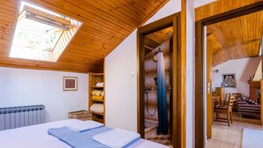 A bedroom with a skylight, a bed with neatly folded towels, a wooden floor, and a view of a bathroom with a shower and a bathtub.