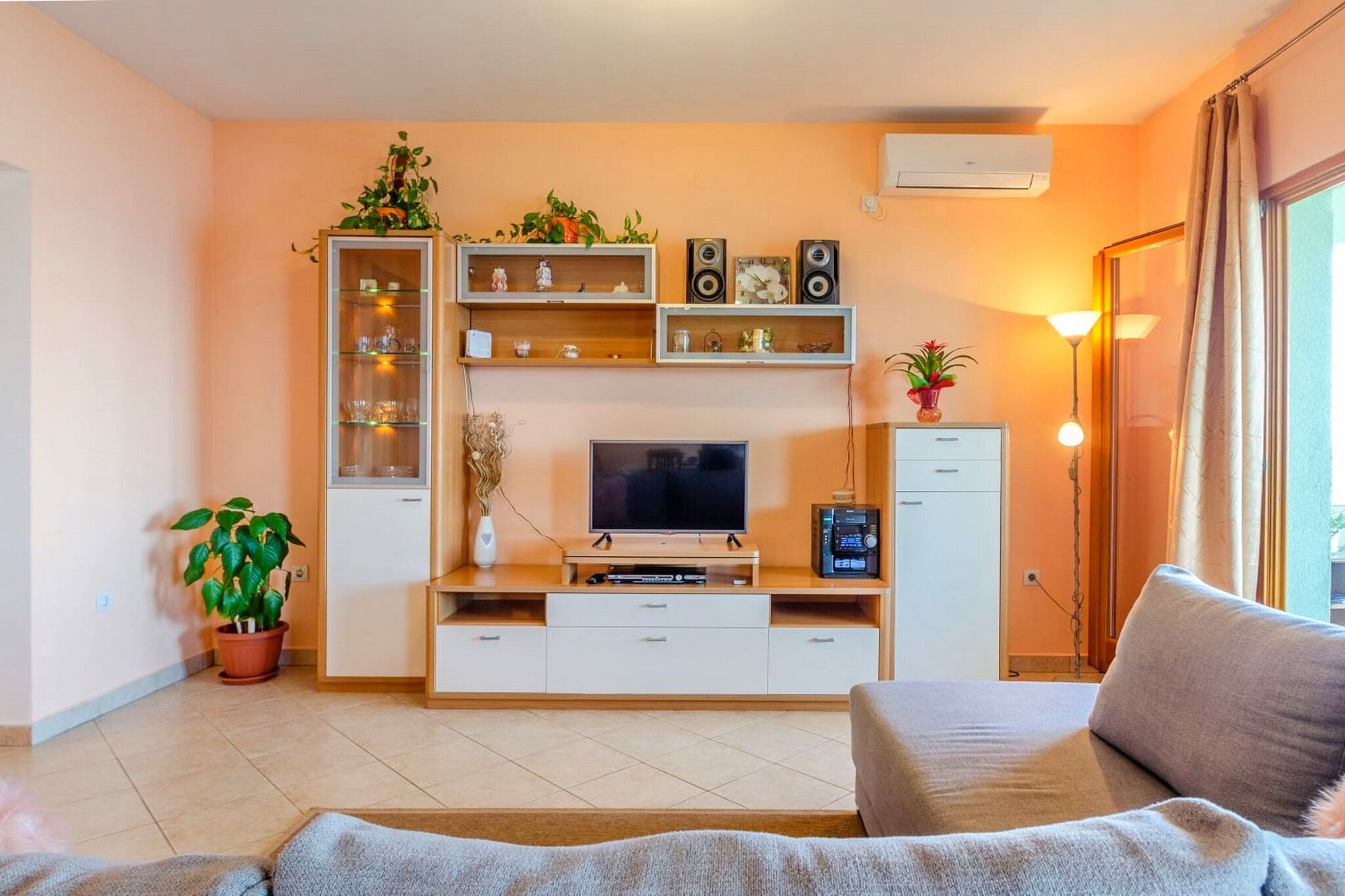 A living room with a TV, shelves, a cabinet, a sofa, and a potted plant.