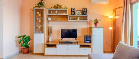 A living room with a TV, shelves, a cabinet, a sofa, and a potted plant.