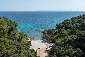 A beach with clear turquoise waters, surrounded by dense green pine trees, and boats parked along the shore.