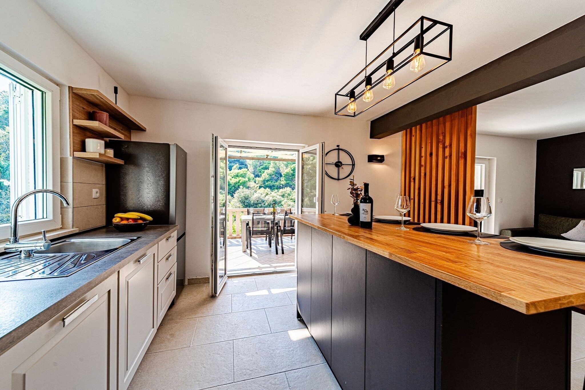 A modern kitchen with a wooden countertop, a built-in oven, and a view to an outdoor dining area.