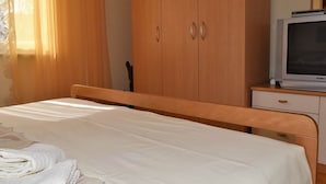 Un dormitorio con cama, armario de madera y televisor sobre una mesita.