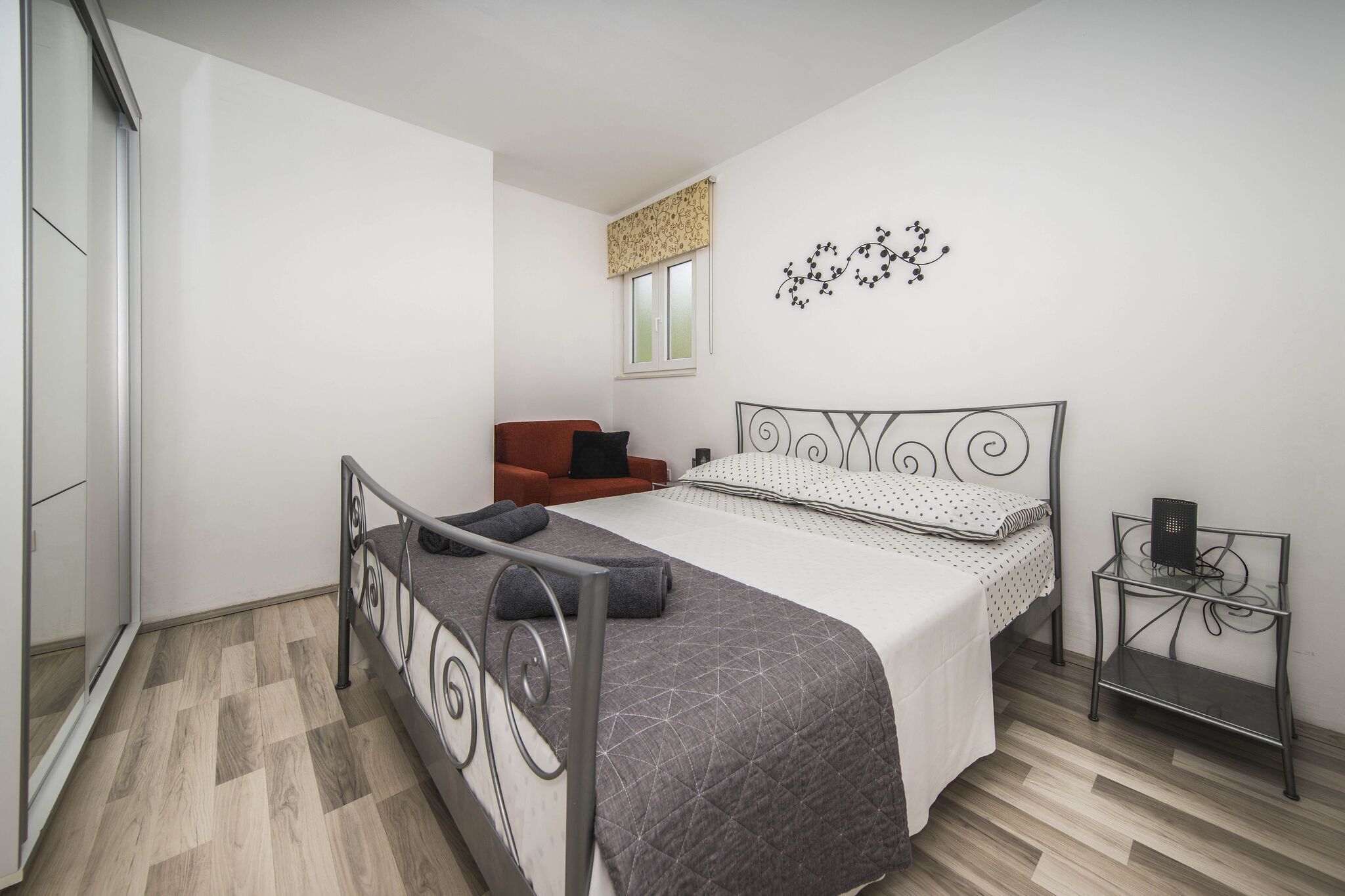 A bedroom with a bed, a chair, a small table, and a window with a curtain.