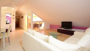 A modern living room with a white sofa, a glass coffee table, and a flat-screen TV on a dark wooden console.