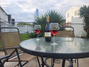 Een ronde glazen tafel met twee stoelen, een fles wijn en twee wijnglazen erop.