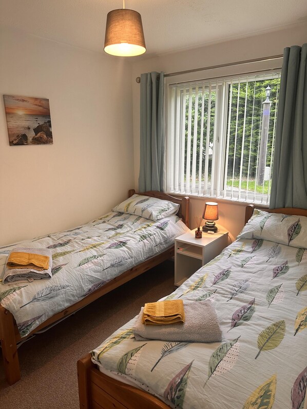 Ein Schlafzimmer mit zwei Einzelbetten, einem Nachttisch mit Lampe, einem Bild an der Wand und einem Fenster mit Vorhängen.