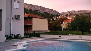Una piscina de borde curvo, un edificio con balcón y montañas al fondo.