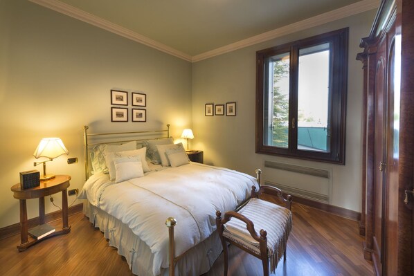 A neatly arranged bedroom with a bed, two bedside tables with lamps, a chair, and a large window. - Villa Paola in Padova (Saonara)