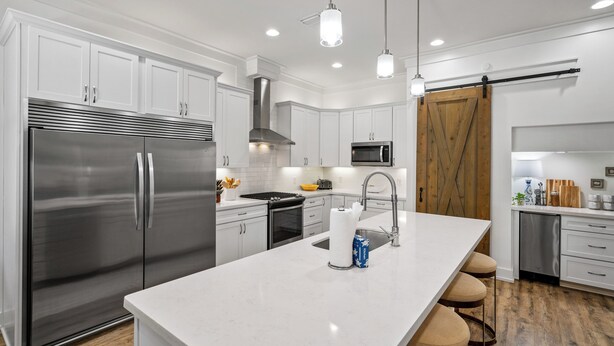 A modern kitchen with white cabinetry, stainless steel appliances, a central island with stools, and pendant lighting. - Gone Coastal | Private Pool | 6-Seater Golf Cart | Arcade Games (Watersound)