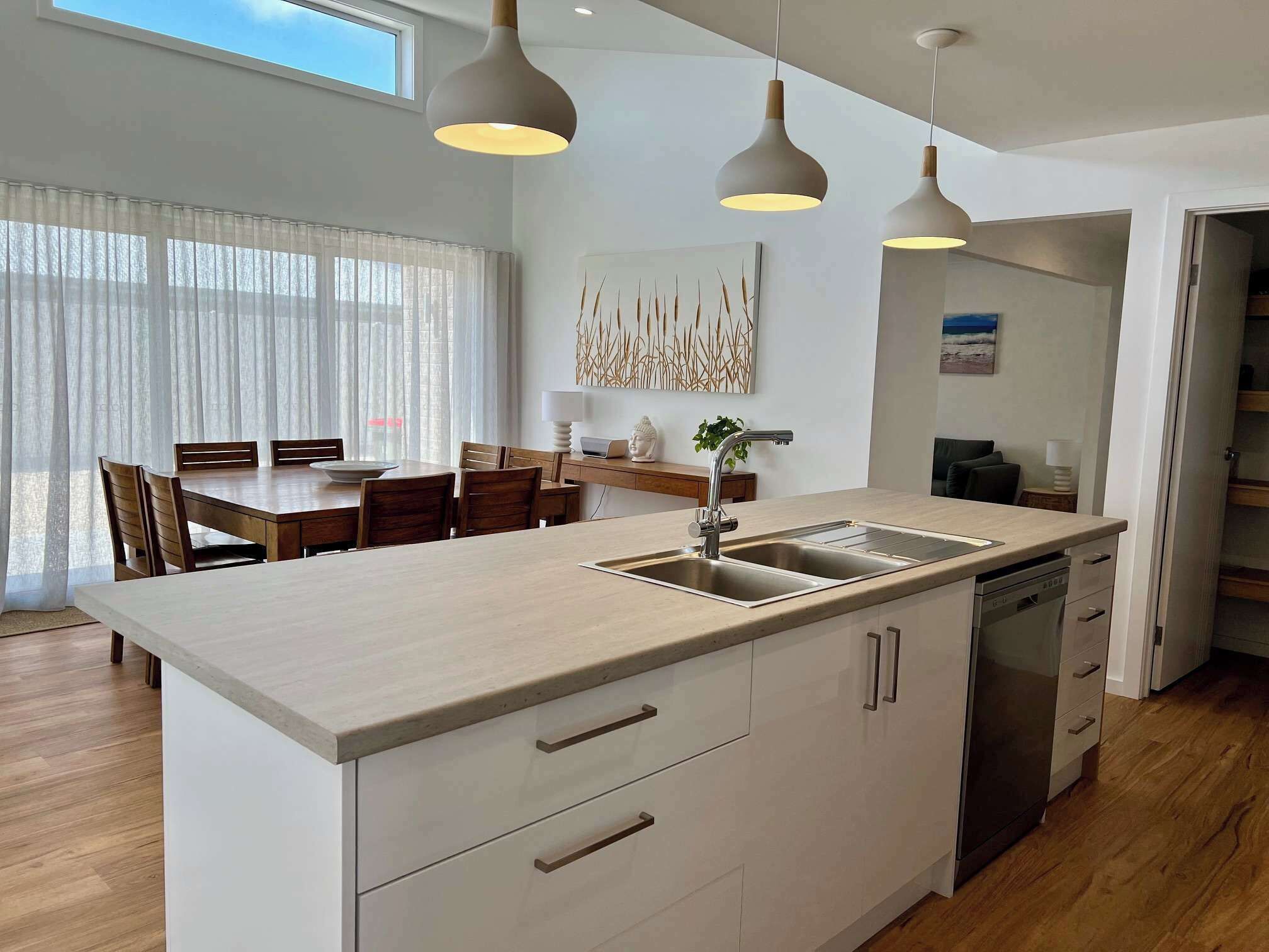 Una cocina moderna con una isla central, un área de comedor con mesa y sillas, e iluminación colgante.